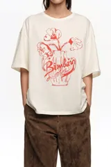 Remera oversize color blanco crudo, confeccionada en algodón, con cuello redondo y mangas cortas. Presenta un estampado frontal en color rojo de un jarrón con flores y el logo de la marca en caligrafía.