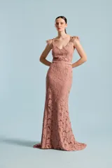 Vestido largo de fiesta de encaje color rosado, con escote en V, tirantes finos decorados con plumas y pedrería, y una sutil falda sirena con pequeña cola.