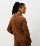 Buzo deportivo de corte oversized en color verde oliva, confeccionado en tejido modal con mezcla de poliéster y elastano. Presenta cuello alto con cierre frontal de cremallera y paneles frontales con textura acanalada. Incluye mangas largas con puños elásticos ajustados.