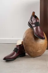 Zapato tipo botineta de cuero color bordó con textura grabada, diseño de punta fina y detalles de elásticos laterales en color negro.
