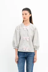 Blusa a rayas verticales grises y blancas con mangas abullonadas y tres lazos rosas en el frente.