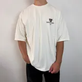 Remera negra de corte oversize con estampa gráfica en la espalda que presenta un oso con anteojos y bandana, acompañada de la frase 'Richer, Louder & Unbothered Than Ever'.
