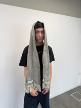 Bufanda larga de tejido trenzado con diseño de cuadros en tonos beige, marrón, negro y blanco. Presenta flecos en los extremos, una grifa de goma con logo en una punta y una etiqueta tejida con logo en la otra.