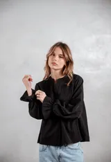 Camisa negra de corte holgado con detalles de bordado tipo broderie en el pecho y mangas largas con puños acampanados.