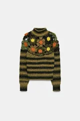 Jersey de punto con cuello subido y manga larga. Presenta un diseño de rayas horizontales en tonos verde y negro, con un panel superior decorado con calados y aplicaciones de flores tejidas en crochet de colores contrastantes.