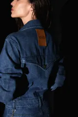 Mono de denim azul con cierre frontal de botones metálicos, cuello camisero, mangas largas y bolsillos delanteros.