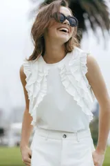 Remera sin mangas blanca con escote a la base y volados aplicados en los hombros.