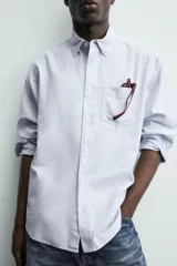 Camisa de corte regular fit confeccionada en tejido de algodón con diseño de rayas verticales. Presenta cuello abotonado, manga larga con puños abotonados, bolsillo plastrón en el pecho y cierre frontal con botones.