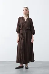 Vestido largo color marrón, de silueta fluida, con escote en V y botones frontales. Presenta cintura elastizada y mangas largas con elástico en los puños.