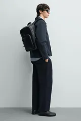Mochila de diseño minimalista en color negro con acabado grabado. Cuenta con compartimento principal con cierre, bolsillo frontal con cierre, asa de mano superior y correas de hombro ajustables y acolchadas. Incluye espacio interior para dispositivos electrónicos y bolsillo de seguridad trasero.