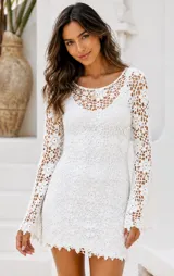 Vestido corto tejido a mano en dos hilos color crudo, con diseño de flores caladas y mangas amplias. Incluye body separado.