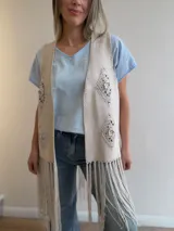 Chaleco beige con efecto gamuza, diseño abierto, apliques de crochet geométricos en relieve y flecos largos en el ruedo.