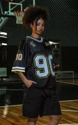 Camiseta estilo jersey de fútbol americano, color negro, con cuello en V ribeteado en blanco y dorado. Presenta el número "90" grande en el frente con borde blanco y dorado. Tiene inscripciones bordadas en el pecho como "L.A." y "Ravers", y el número "9" en la manga.