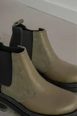 Botas tipo Chelsea con diseño bicolor en tonos negro y verde oliva. Presentan paneles laterales elásticos, suela track robusta y tirador trasero.