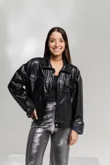 Chaqueta negra de cuero sintético con cuello camisero, cierre frontal con botones a presión, dos bolsillos con solapa en el pecho y puños abotonados.
