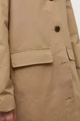Trench impermeable color beige con cuello camisero en contraste de color marrón oscuro. Presenta cierre frontal con botones, bolsillos delanteros con solapa y mangas largas.