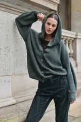 Cardigan de punto con capucha, de calce relajado y mangas amplias. Presenta cierre frontal con botones y diseño acanalado.