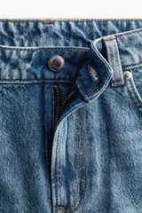 Jean de tiro alto confeccionado en denim de algodón lavado con diseño de cinco bolsillos, piernas rectas y holgadas, y detalles de roturas en las rodillas.