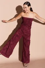 Pantalón de lino color bordó con volados decorativos en forma de espiral a lo largo de las piernas.