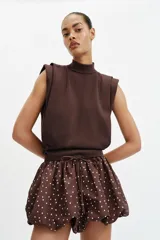 Falda pantalón de tiro medio con diseño abullonado, confeccionada en tela satinada color marrón con estampado de lunares blancos. Cuenta con cintura elástica ajustable mediante cordones.