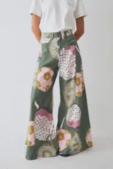 Pantalon de corte wide leg y tiro alto, confeccionado en tela con estampado deportivo que incluye pelotas de futbol y raquetas de tenis en tonos verde, rosa y beige.