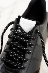 Zapatillas urbanas de cuero negro con puntera y talón de gamuza negra, detalles en cuero con textura de reptil y suela de goma color caramelo.