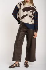 Sweater de punto con diseño combinado, presentando un estampado de manchas de vaca en el cuerpo y mangas con rayas horizontales en tonos azul y marrón. Posee cuello redondo y puños acanalados.