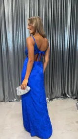 Vestido largo azul eléctrico, con corpiño de lentejuelas y falda larga con textura floral en relieve. Posee tirantes finos y escote recto.