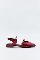 Zuecos destalonados color rojo charol, de punta cuadrada y tiras finas con hebillas ajustables. Cuentan con taco de 2,5cm de alto.