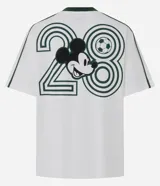 Remera boxy de algodón color blanco, con cuello redondo y ribete verde oscuro, manga corta con líneas decorativas en los hombros, y estampado frontal deportivo de Mickey Mouse con tipografía.
