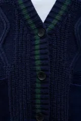 Sacón de punto con frente y espalda en tejido de ochos color azul marino, con detalles de rayas verdes en el borde. Las mangas son de tela de jean azul oscuro. Presenta cierre frontal con botones y bolsillos laterales.