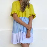 Vestido corto con corte debajo del busto, mangas cortas con volados, parte superior amarilla, sección central celeste y ruedo blanco.