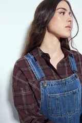 Camisa tipo leñadora de corte oversize, con estampado de cuadros en tonos negro y marrón. Presenta cuello clásico, cierre frontal con botones y mangas largas con puños abotonados.