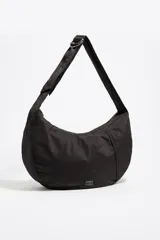 Bolso tipo media luna de nylon negro, con correa ajustable para llevar al hombro o cruzado. Presenta costuras verticales que le dan estructura y un pequeño logo de Bimba y Lola en la parte inferior central.
