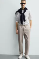 Pantalón jogger color beige de tejido transpirable y elástico con cintura elástica ajustable con cordón, bolsillos frontales y bajo con vuelta.
