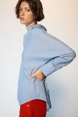 Camisa de manga larga en color celeste con estampado de rayas finas, cuello solapa y escote en pico con detalle de solapa frontal. Presenta puños abotonados y bajo asimétrico.