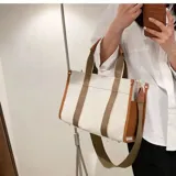 Bolso tipo tote en lona beige con detalles en negro y tiras de hombro blancas y negras. Cuenta con correa ajustable y desmontable.