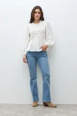 Camisa de color crudo con detalle de fruncido en el pecho, cuello redondo con volado sutil, cierre frontal con botones y mangas largas abullonadas con puños elásticos.