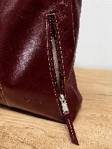Mochila de cuero vacuno marrón con acabado pulido, solapa en forma de V y costuras decorativas. Cuenta con cremalleras laterales y asas ajustables.