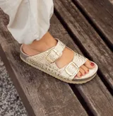 Sandalias bajas doradas con estampado de piel de cocodrilo, dos tiras anchas con hebillas doradas ajustables y plantilla de cuero.