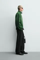 Campera verde oscuro de corte cropped y tejido técnico, con cuello alto, cierre frontal de cremallera con tirador circular, bolsillos ribeteados y puños y dobladillo elásticos.