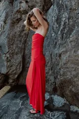 Vestido largo de fiesta color rojo, con escote corazón y diseño palabra de honor. Presenta detalles de drapeado lateral y una superposición de tela con lazada en la cintura, con falda de corte evasé.
