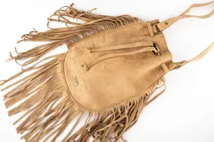 Cartera tipo bucket bag color camel, confeccionada en material sintético con acabado gamuzado. Presenta un diseño decorado con flecos largos en todo el contorno, cierre mediante cordón ajustable y correa larga regulable.