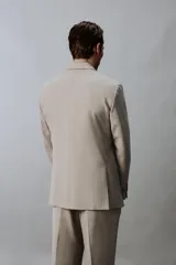 Blazer slim fit de color beige, confeccionada en tejido con lana. Presenta cuello con solapas de muesca, cierre frontal de un botón, bolsillos laterales con solapa y bolsillo de vivo en el pecho.