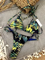 Conjunto de bikini con estampado de hojas de palmera en tonos verde, amarillo y negro. El corpiño es de triángulo con tirantes finos y la bombacha es colaless con tirantes ajustables.