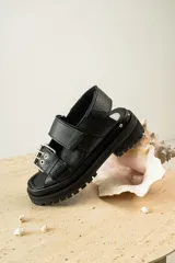 Sandalias negras de cuero con diseño de plataforma dentada, tiras ajustables con hebillas metálicas y detalle de tachas plateadas en el lateral de la suela.