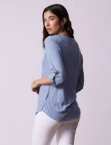 Blusa Ninety color beige con textura, cuello base con escote en V y abertura central con botones. Tiene un bolsillo en el pecho y mangas 3/4 regulables con presilla y botón.