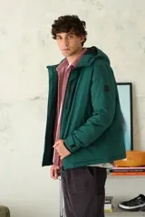 Campera técnica de color verde oscuro, con capucha ajustable, cierre frontal con cremallera y bolsillos laterales con cierre. Presenta puños ajustables con velcro y un diseño acolchado ideal para climas fríos.