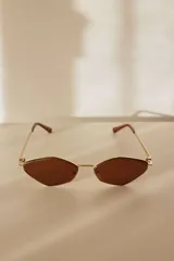 Lentes de sol con montura metálica dorada y cristales de forma geométrica (diamante/hexagonal) en tono marrón. Las patillas son doradas con puntas negras.