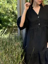 Vestido corto de lino color beige claro, con cuello mao, escote con botones de nácar, mangas tres cuartos con volados y ruedo con volado.